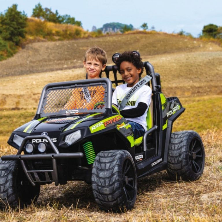 Two children driving a black and green electric ride-on toy car outdoors